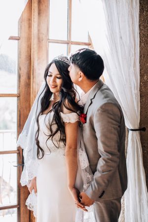 Tucson wedding portrait of a bride and groom holding hands near tall windows with warm natural light.