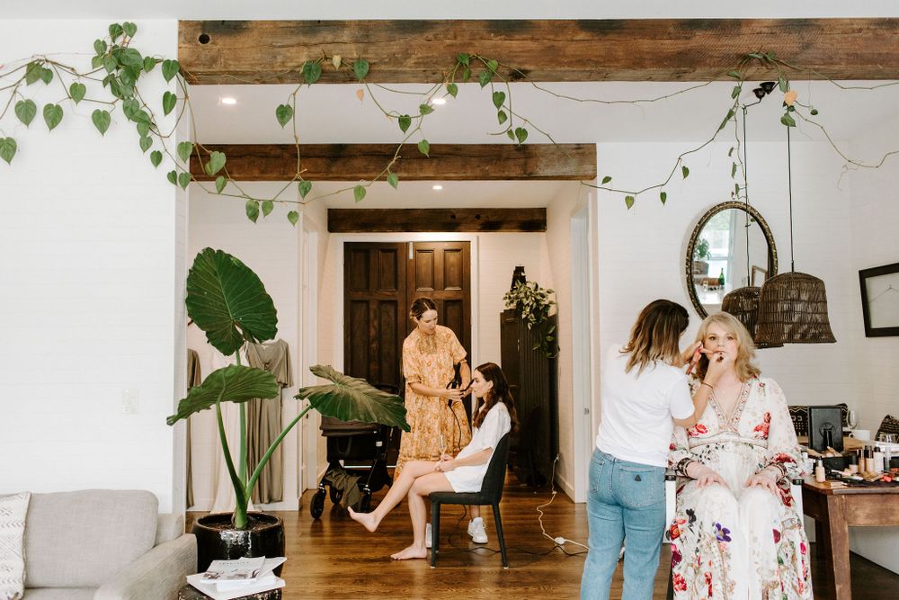 Candid moment of wedding preparation in sunny room with rustic wooden beams and greenery.