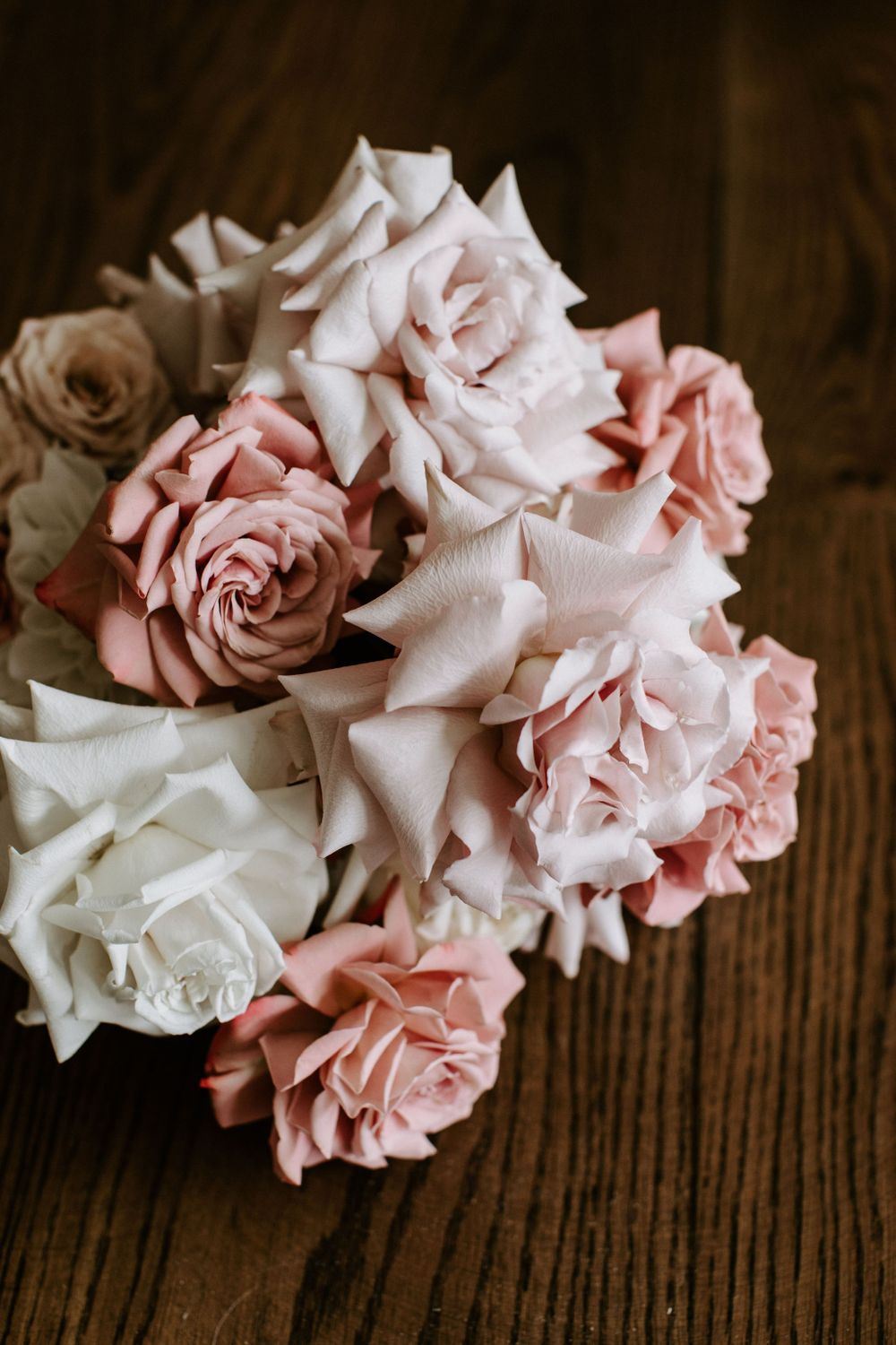 A romantic bouquet of pink and white roses arranged on a dark wooden surface.