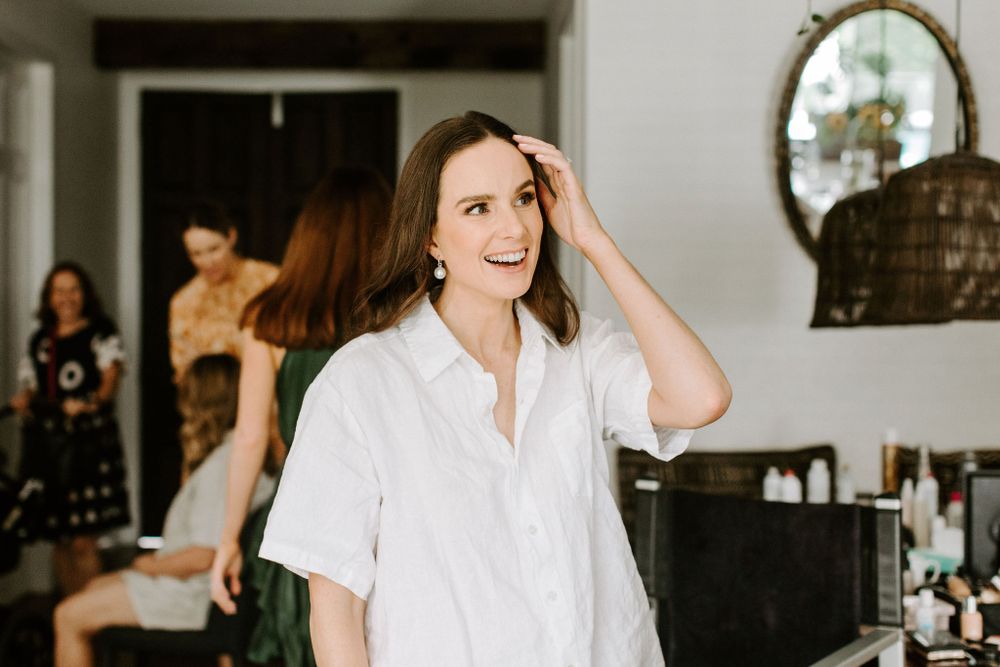 Woman in white shirt touches her hair while others prepare in background.