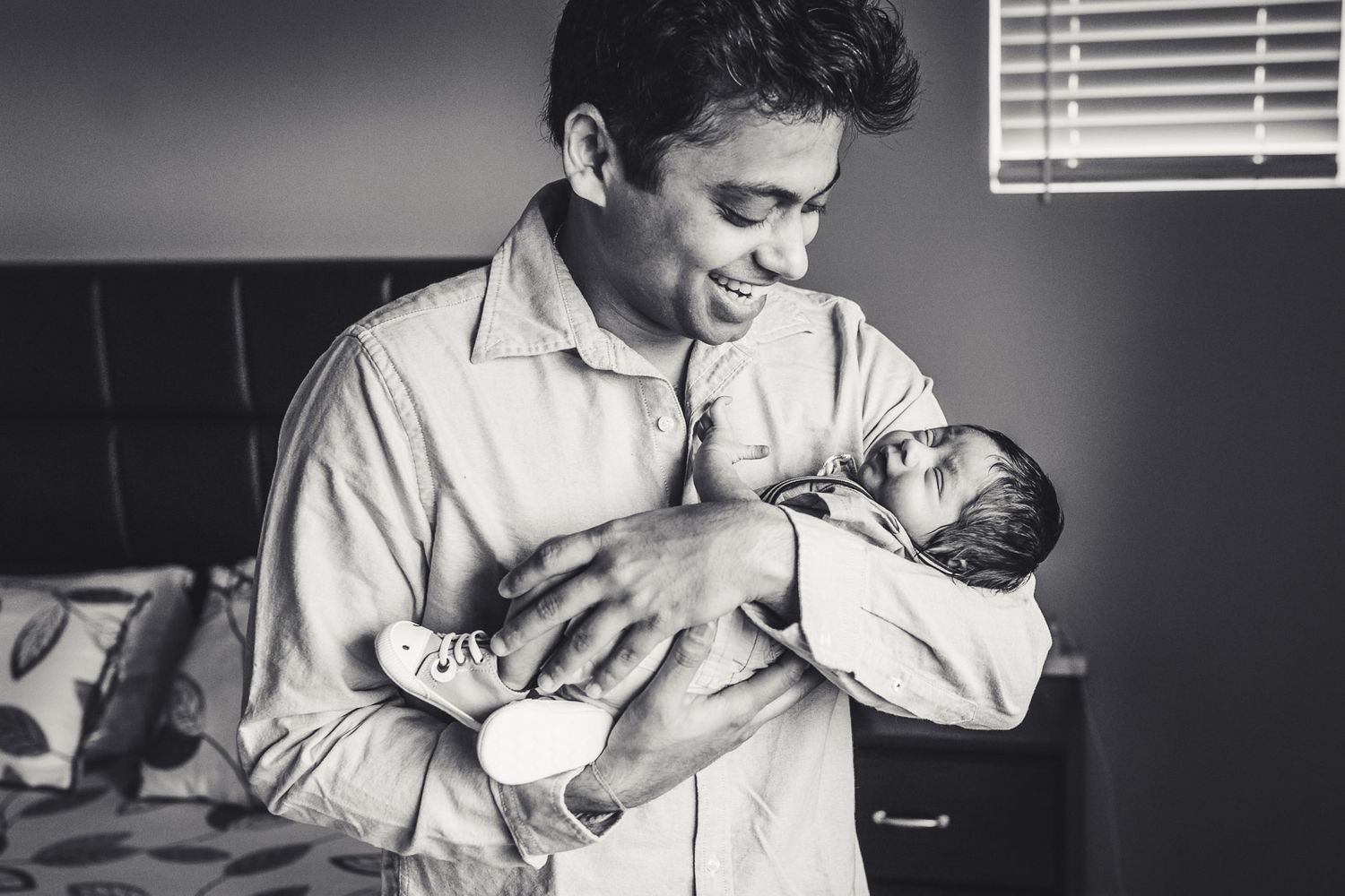 Black and white photo of father smiling while holding newborn son