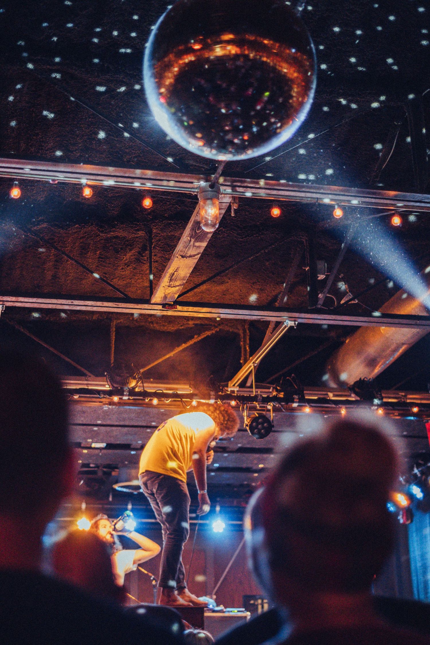 Andy Frasco standing on piano while singing, disco ball hangs from ceiling