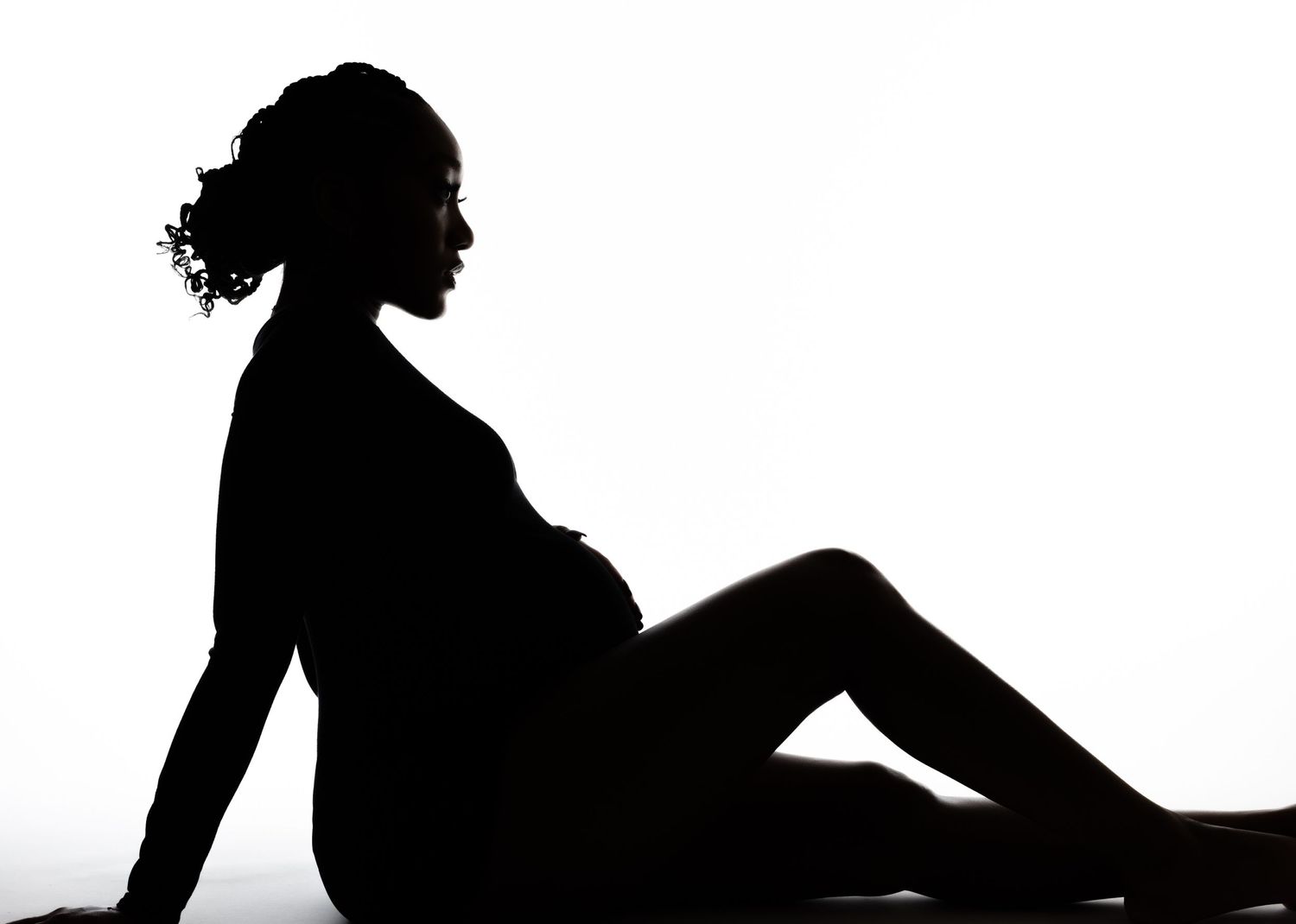 Artistic silhouette of pregnant woman reclining in profile against white background.