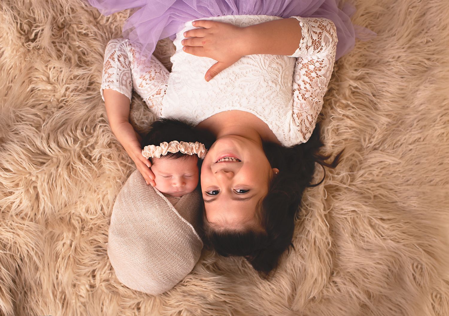 Big sister hold baby sister while baby is wrapped up and warm in Alvin, Tx photography studio