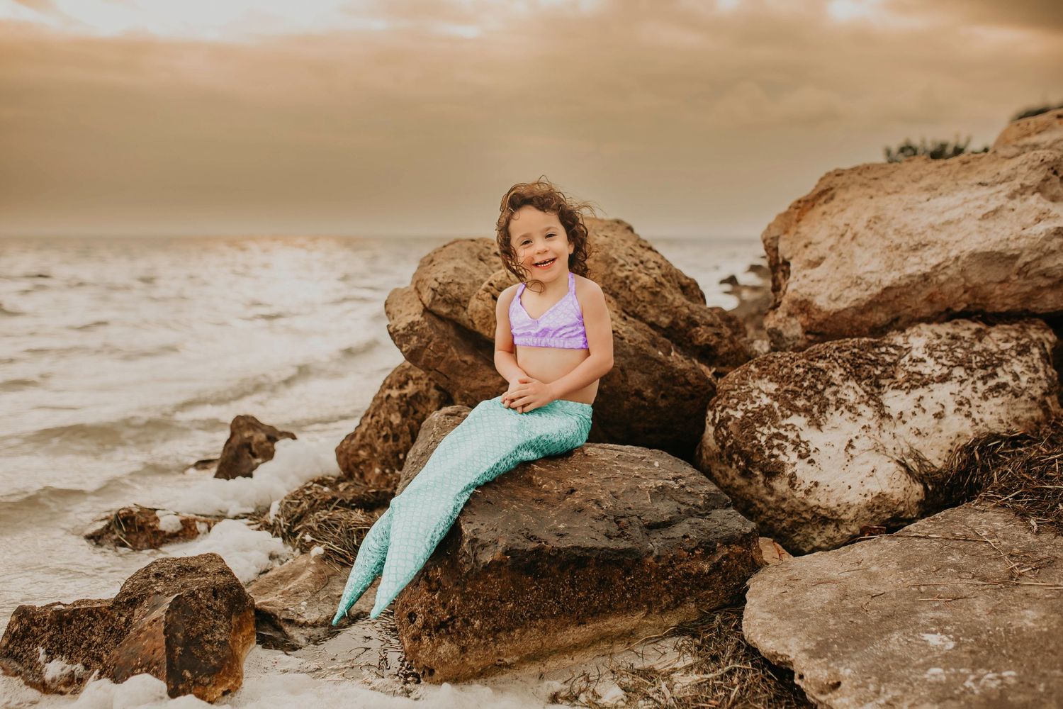 Coastal sunset scene with rocks and ocean waves in warm sepia tones.