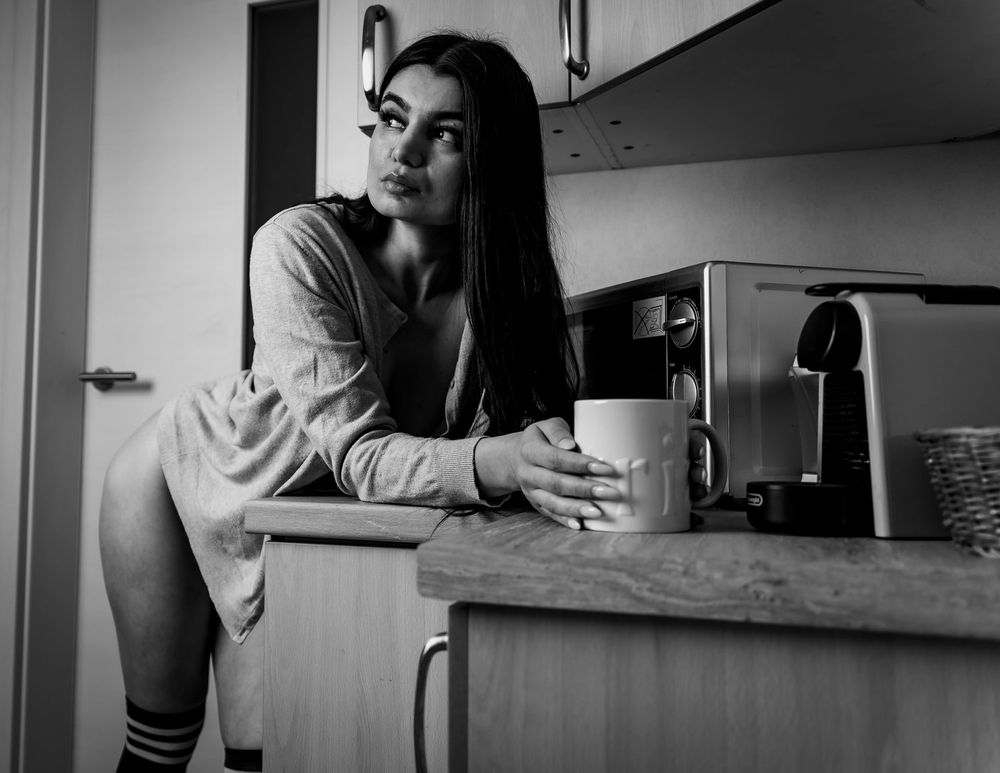 Monochrome kitchen scene with relaxed pose and coffee mug.