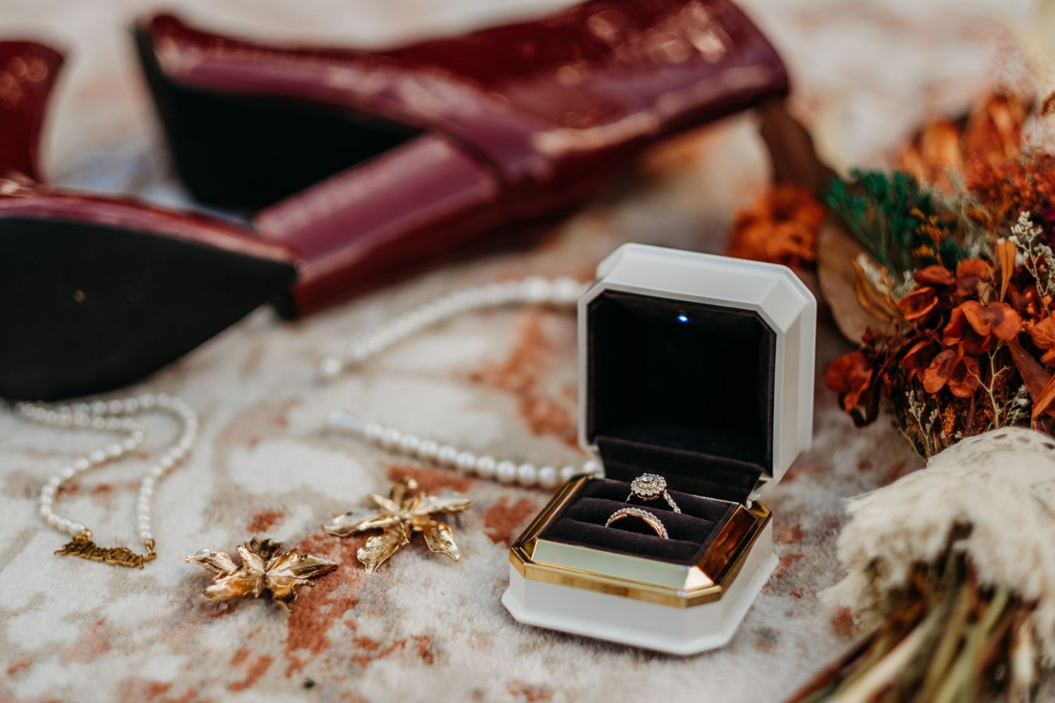 Wedding rings and accessories styled with burgundy leather items and dried floral elements.