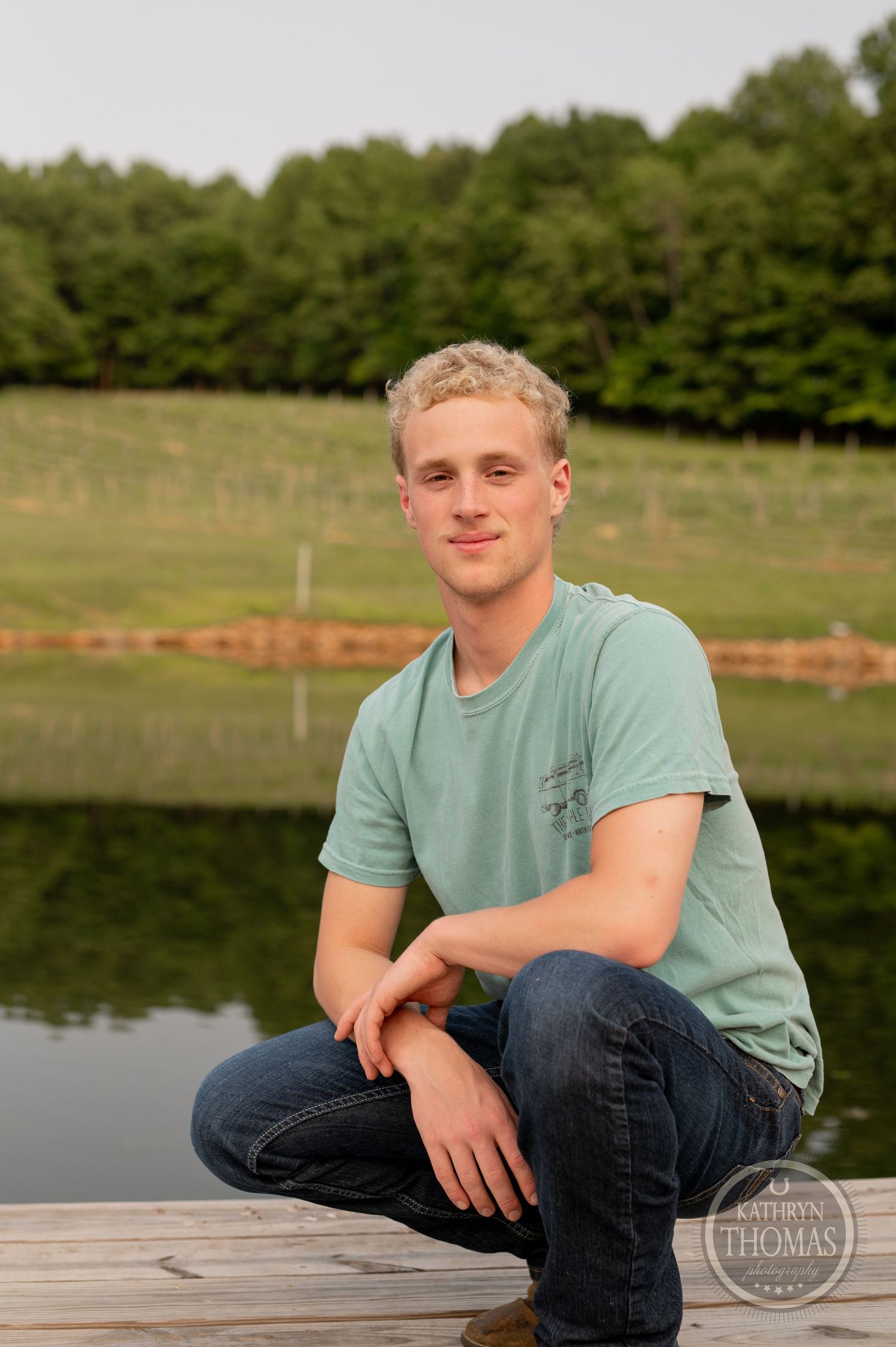 Casual outdoor portrait at a lake with green trees and natural lighting in the background.