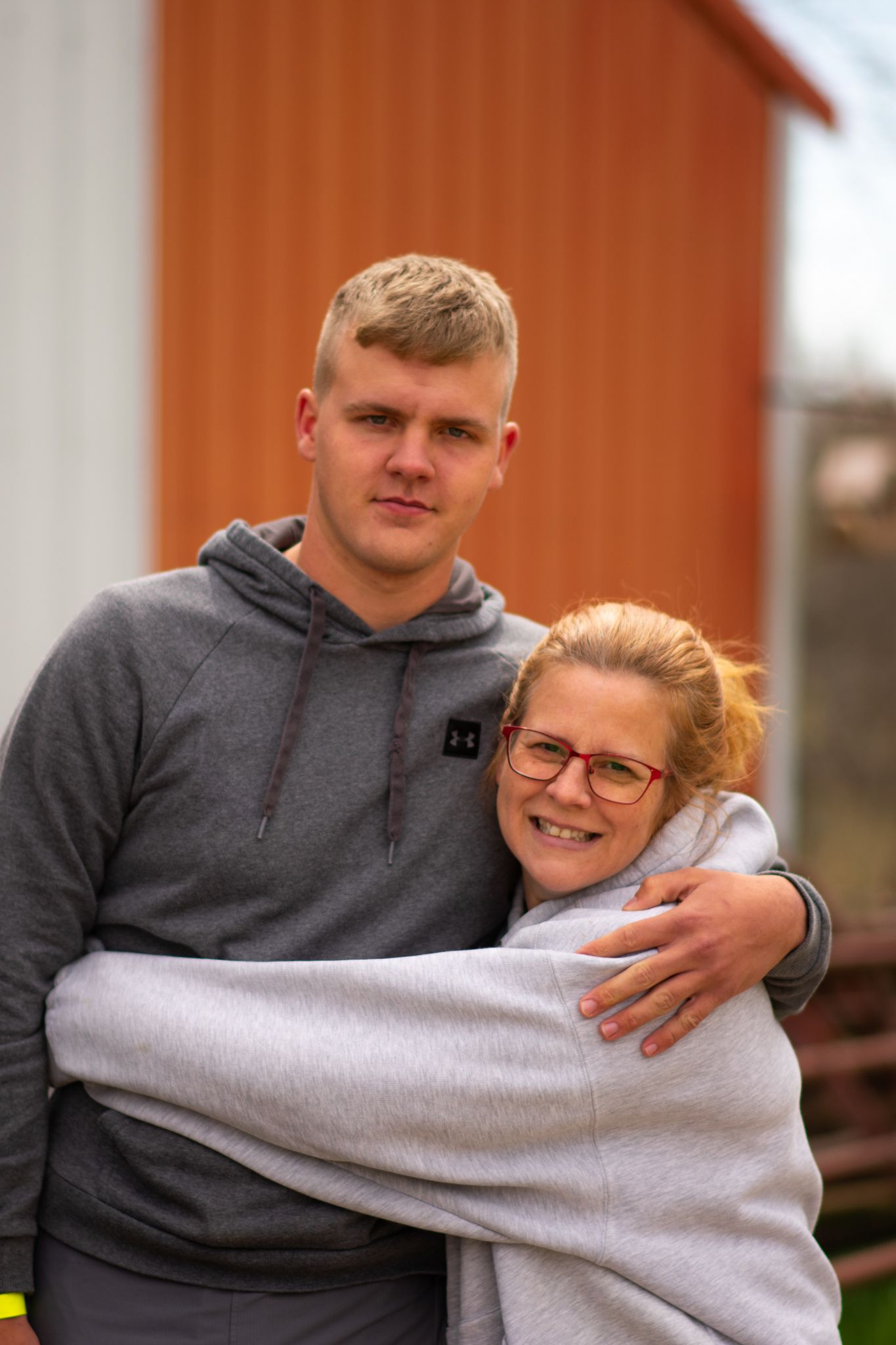 Two people sharing a warm embrace outdoors in front of an orange building.