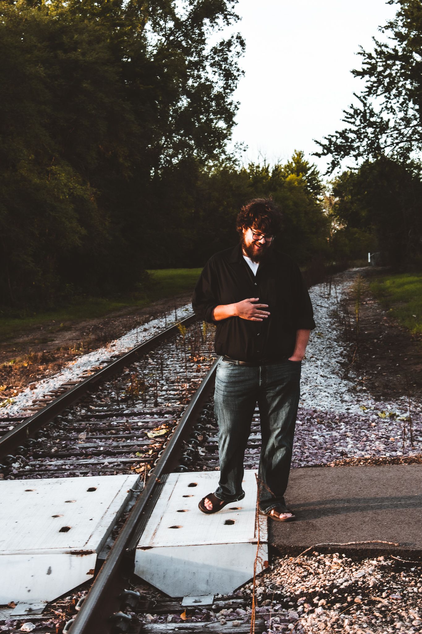 Figure standing on train tracks during golden hour in natural setting.