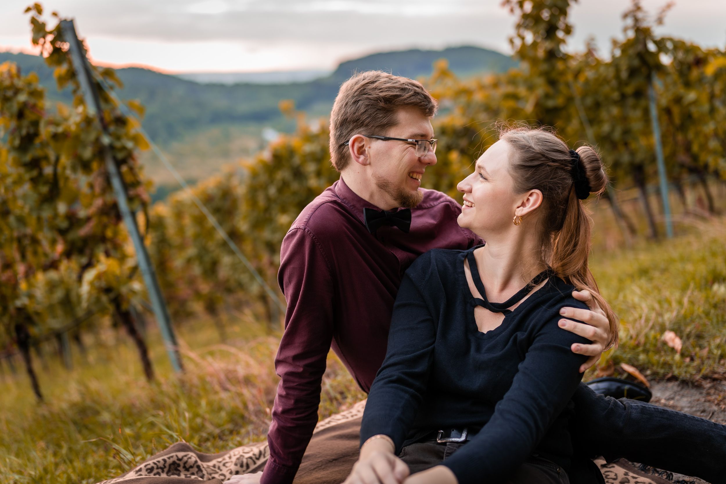 Couple sharing a tender moment while sitting among vineyard rows during fall season.
