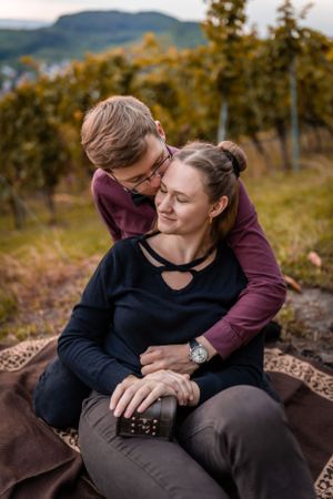 Cozy autumn engagement session on blanket in hilltop vineyard setting.