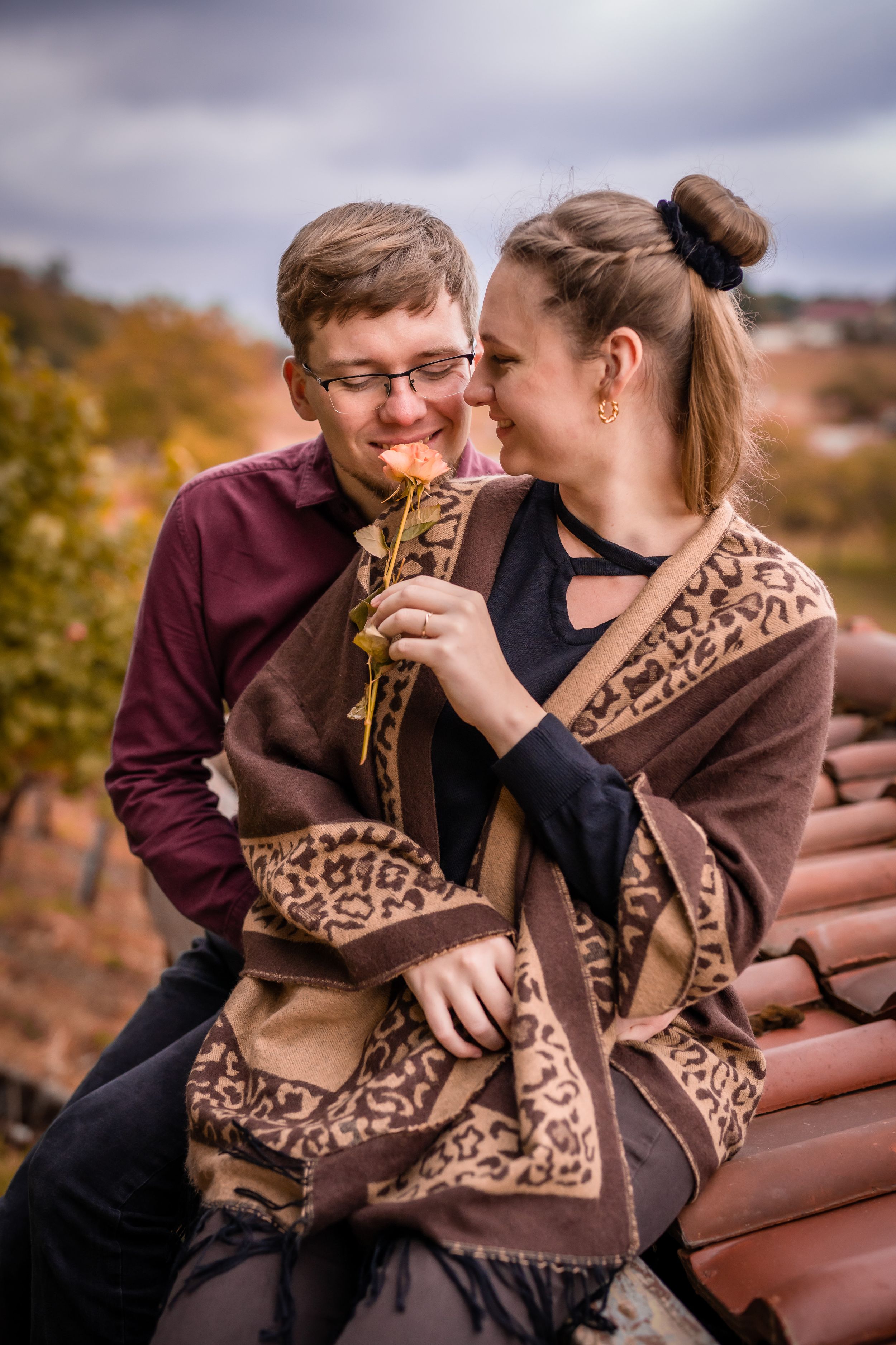 Couple wrapped in patterned blanket sharing intimate moment in autumn vineyard setting.