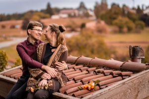 Romantic autumn moment with couple sitting on rustic rooftop with scattered orange pumpkins.