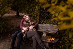 Couple relaxing together on rustic wooden bench surrounded by autumn foliage in romantic outdoor setting.