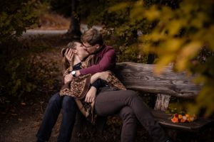 Intimate moment shared on wooden bench with autumn leaves and pumpkins in background.