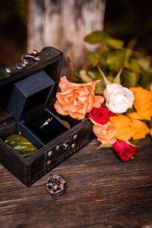 Vintage wooden box with ring and colorful roses arranged on dark wooden surface.