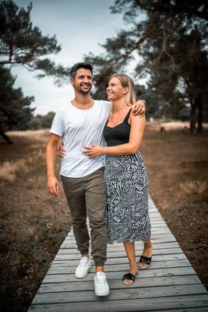 A couple sharing a joyful moment while walking on a wooden boardwalk among pine trees.