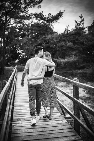 A couple walking arm in arm on a wooden bridge in a tranquil forest setting.