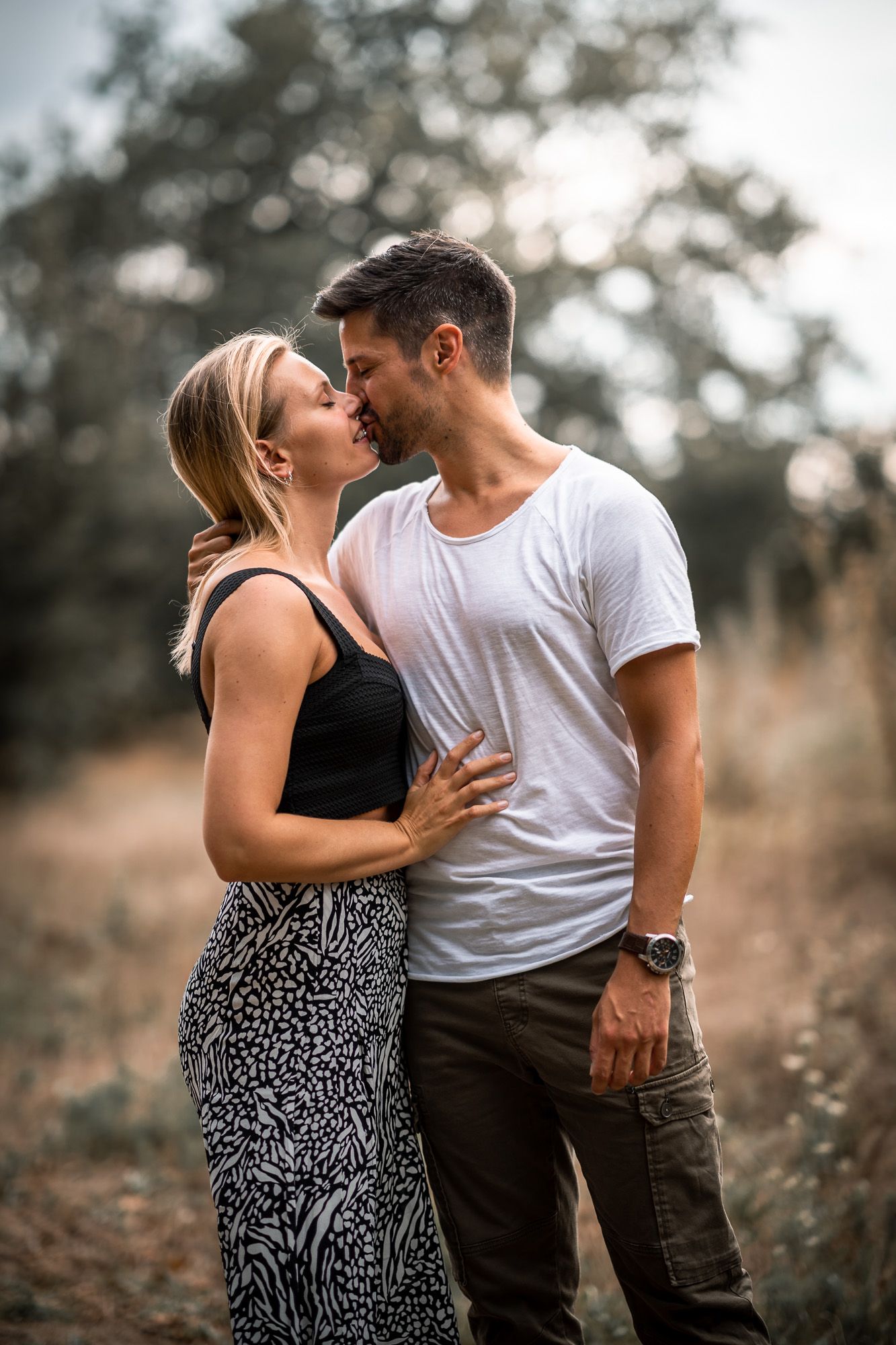 An intimate moment between a couple in casual attire against a softly blurred natural background.