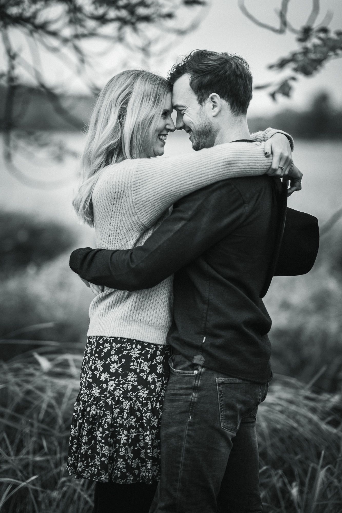 A black and white portrait of a couple sharing an intimate embrace in tall grass.
