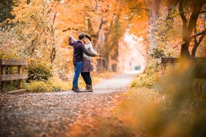 A couple dancing among vibrant autumn foliage on a tree-lined path.