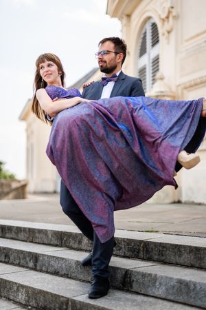 Elegant couple poses on grand stone steps with flowing purple gown creating dramatic movement.