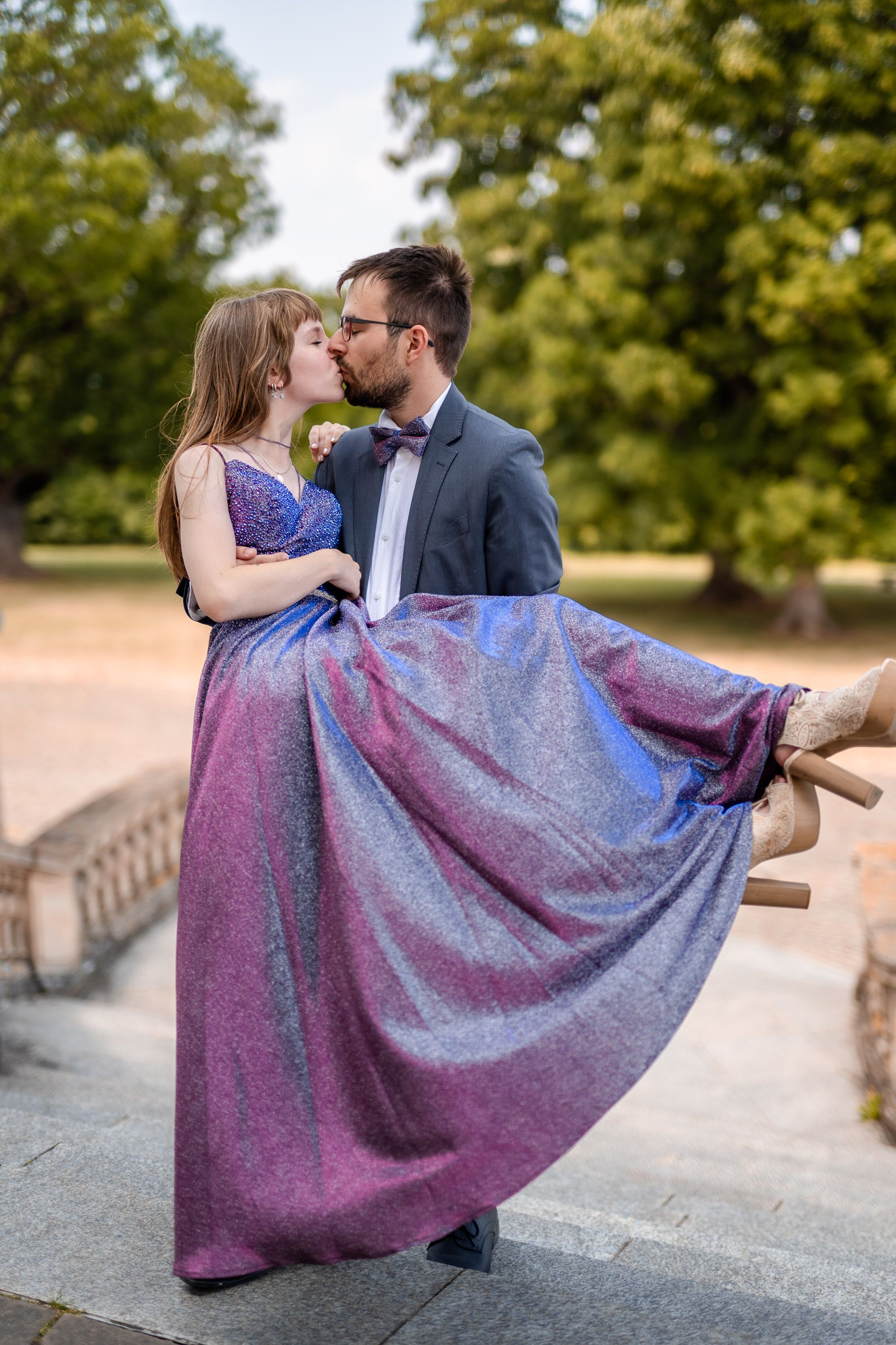 Romantic moment captured on stone steps with flowing purple dress and formal attire.