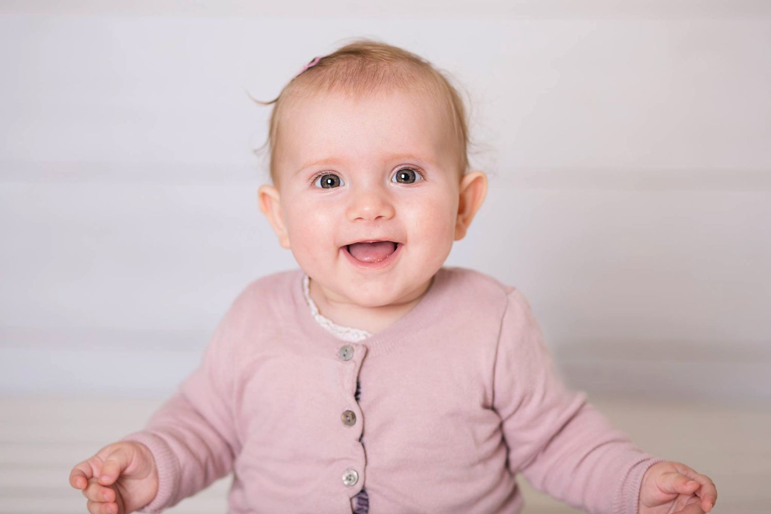 En smilende baby i en lyserød cardigan sidder mod en lys baggrund.