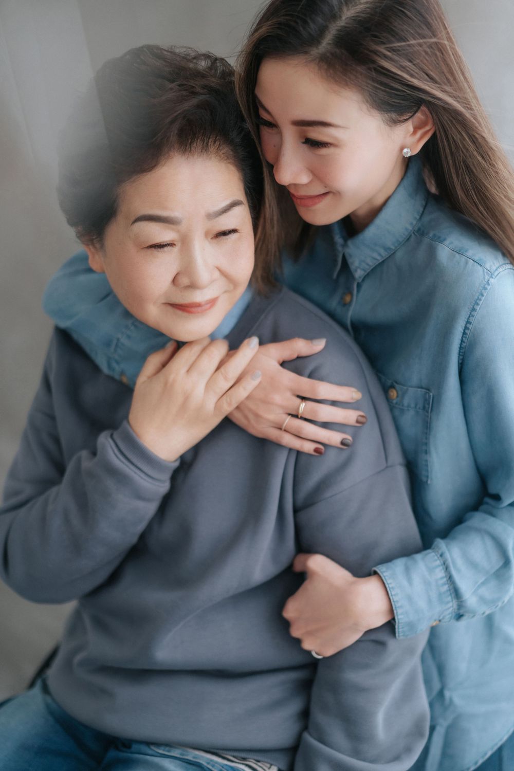 Two generations share an affectionate embrace while wearing casual denim and grey clothing.