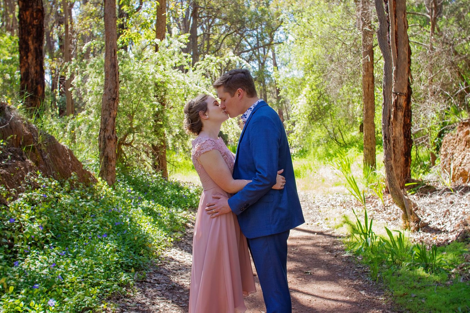 bride and groom wearing pink and navy kissing in forest
