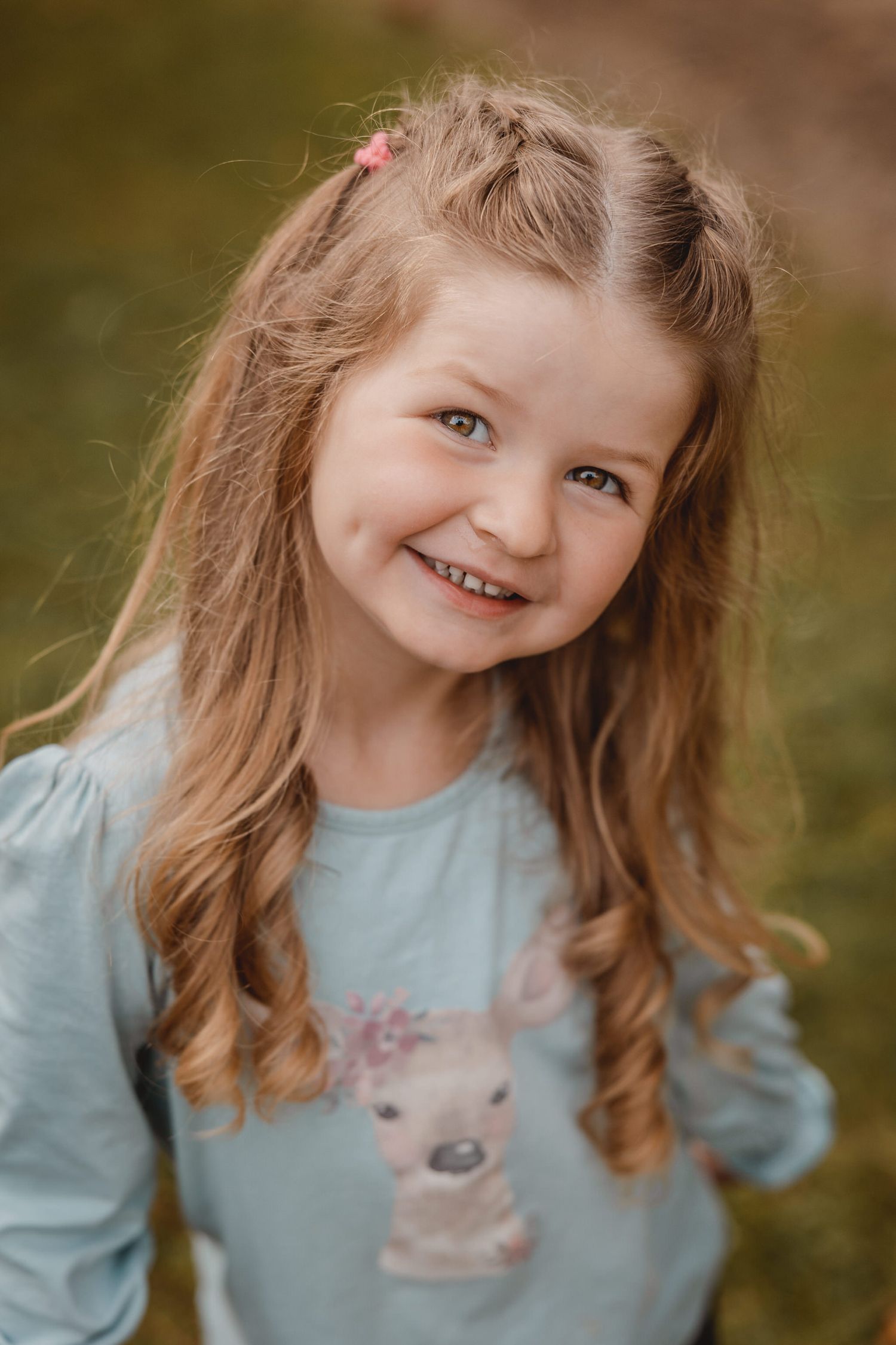 Child in light blue sweater smiling during outdoor portrait session.