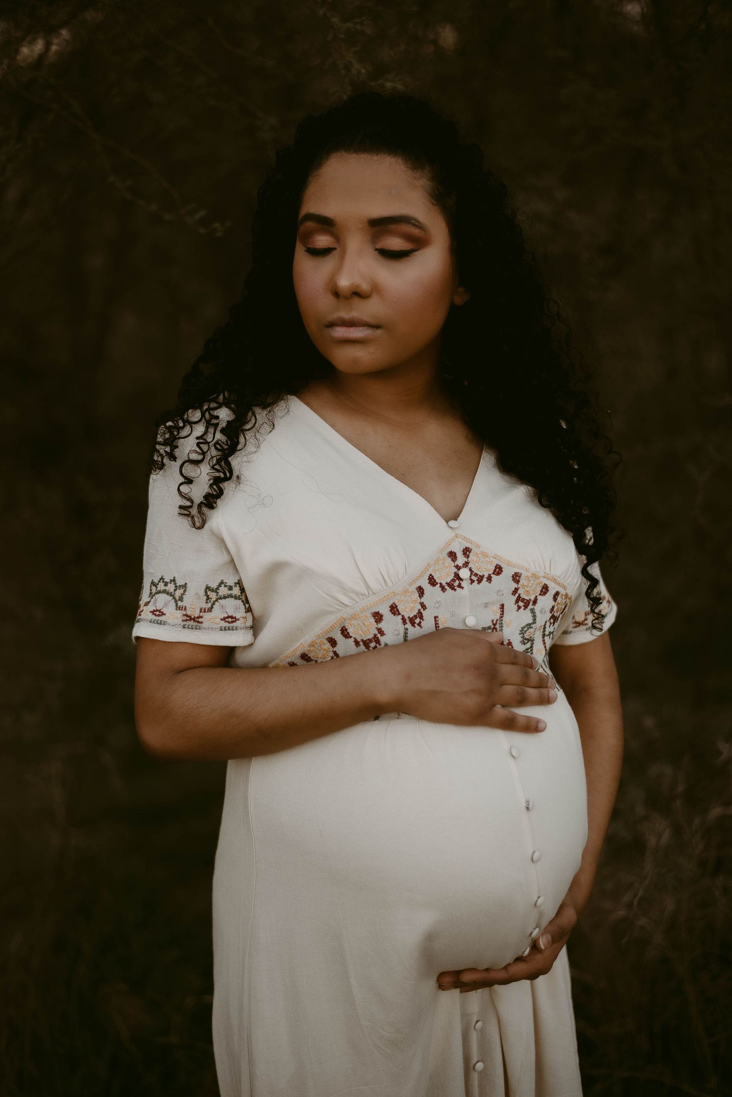 Artistic maternity photograph with moody lighting showing intricate dress details.