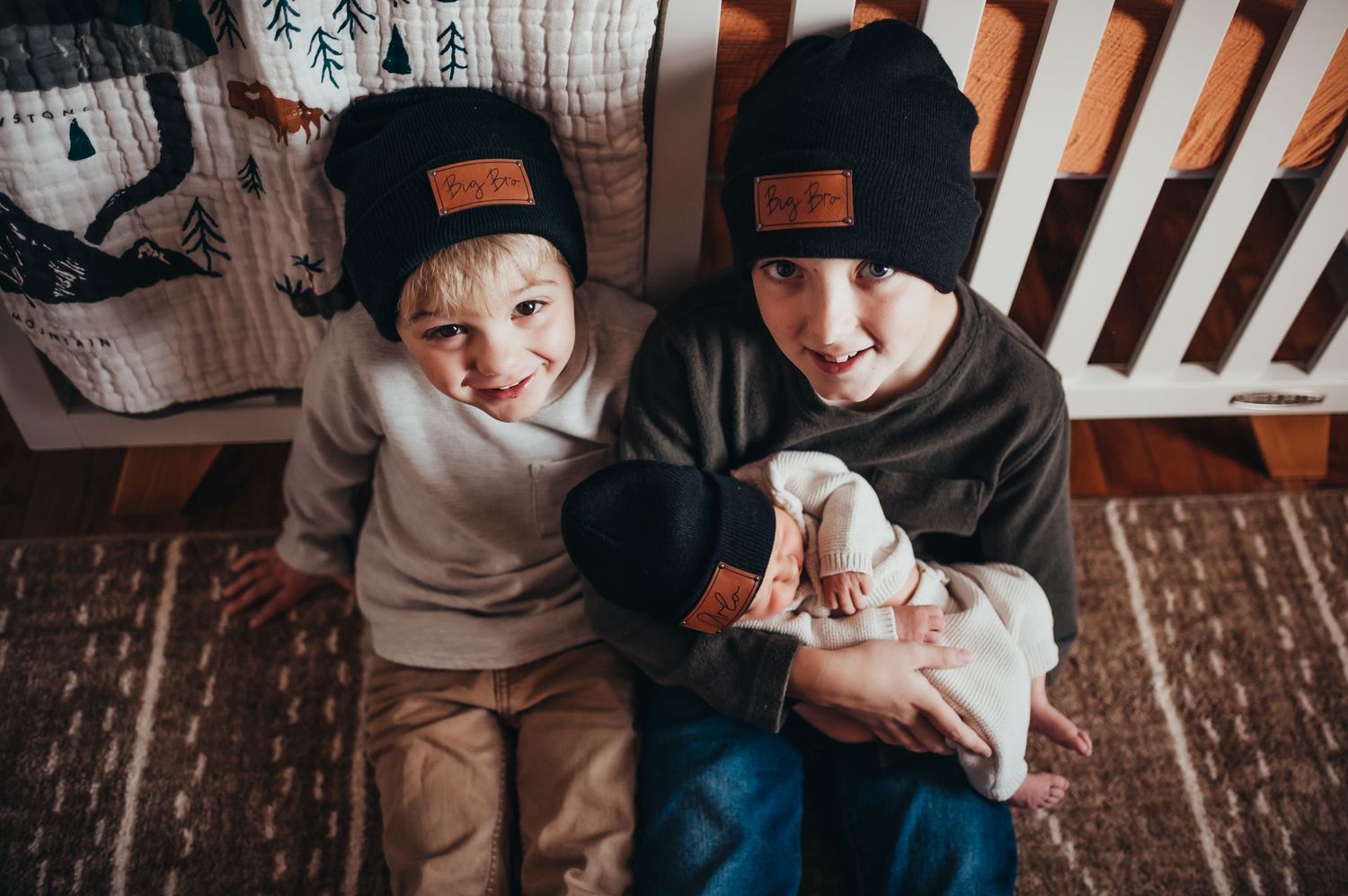 2 boys in big bro beanies hold newborn little brother in matching beanie in the nursery for lifestyle newborn session