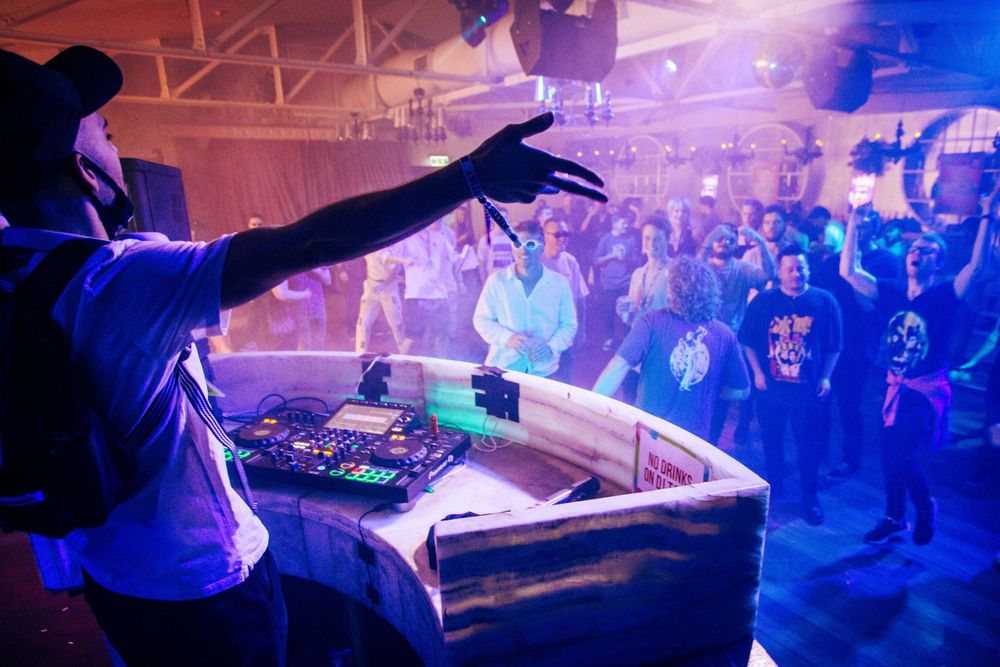 DJ performs for energetic crowd under blue lights at packed nightclub event.