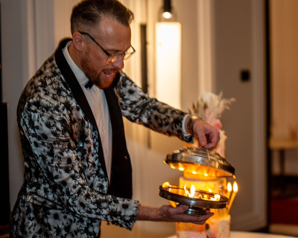 A person in a patterned blazer and bowtie pours a drink from an illuminated cocktail shaker.