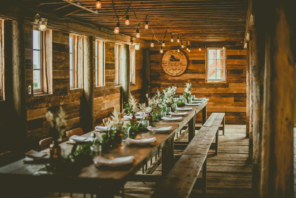 Rustic wooden reception hall with long tables decorated with greenery and string lights.