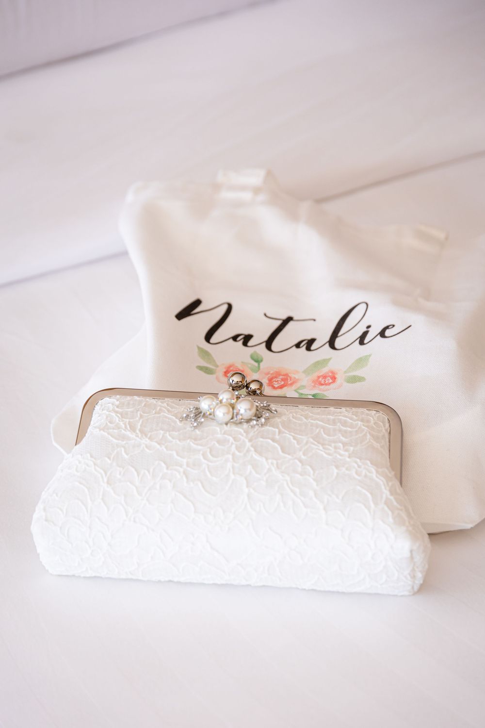 White lace bridal clutch purse with personalized name tag on white wooden background.