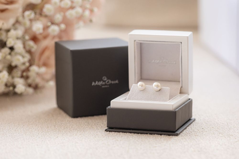 Pearl stud earrings displayed in a gray velvet jewelry box.