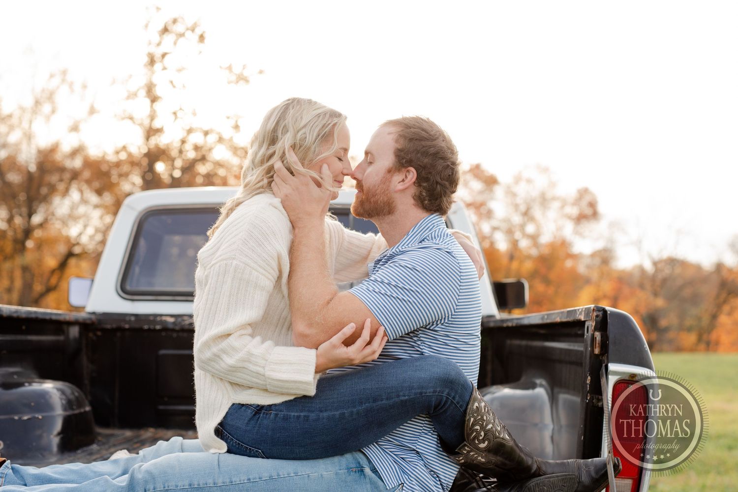 Couple sharing romantic moment in back of pickup truck during golden hour.