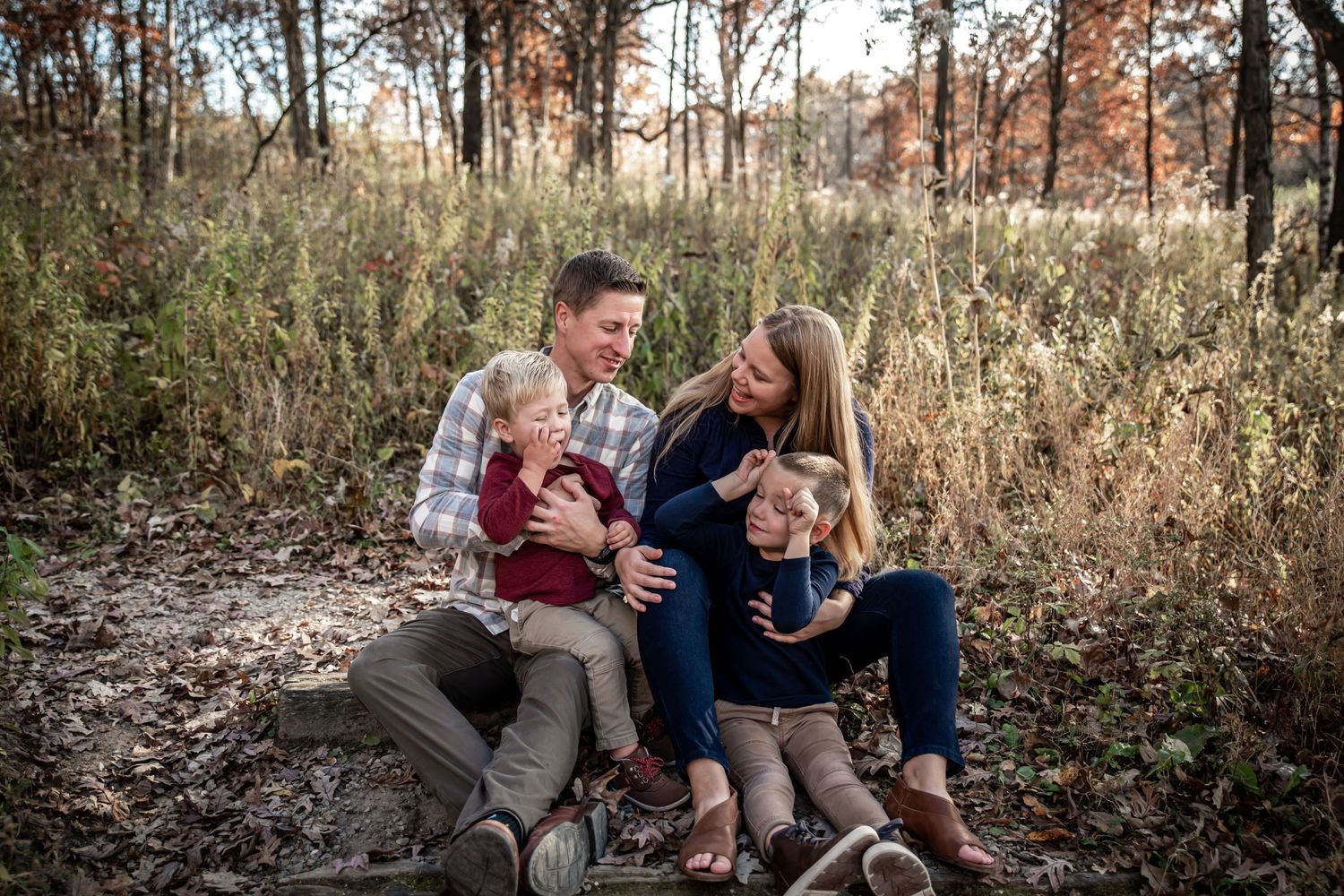 A family sits together on fallen logs in a wooded area during golden hour.