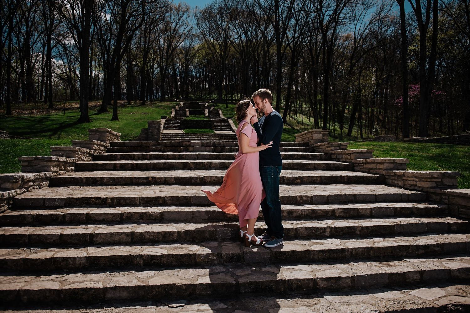 A romantic moment captured on stone steps in a park setting.