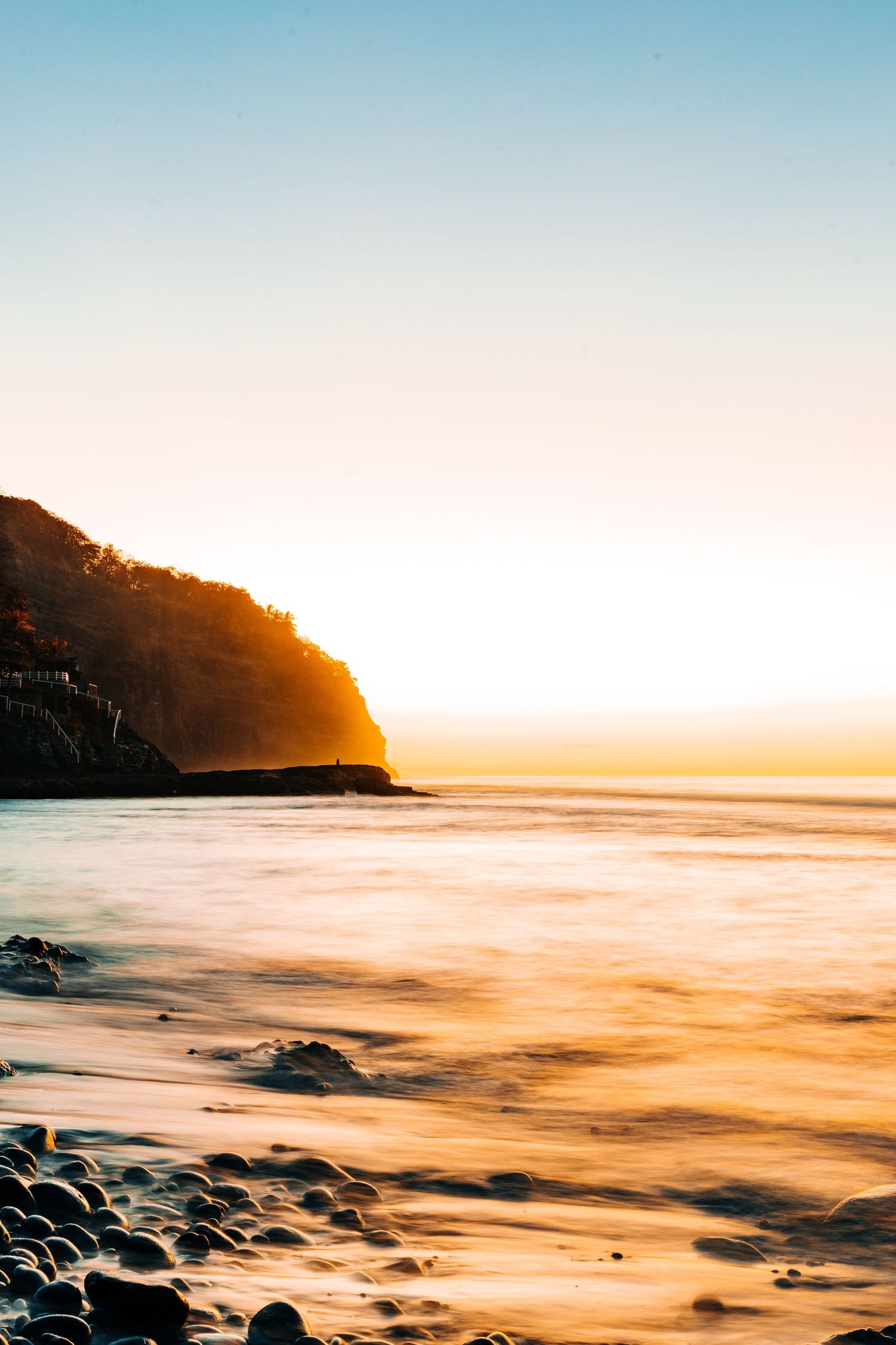 Dramatic sunset over a rocky coastline with golden light reflecting off the ocean waves.