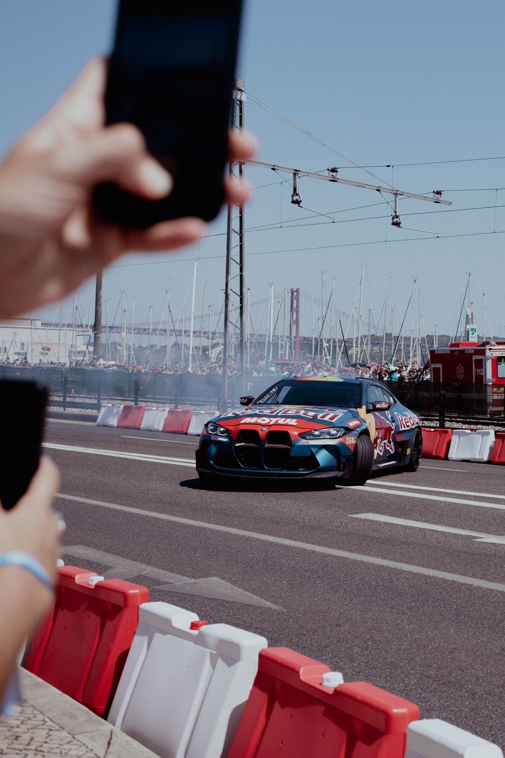 Red Bull BMW M4 drifting on a race track while spectators capture photos on their phones.