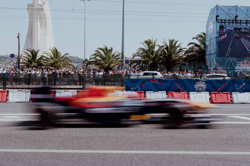 Motion blurred shot of a race car speeding past palm trees and spectator barriers.