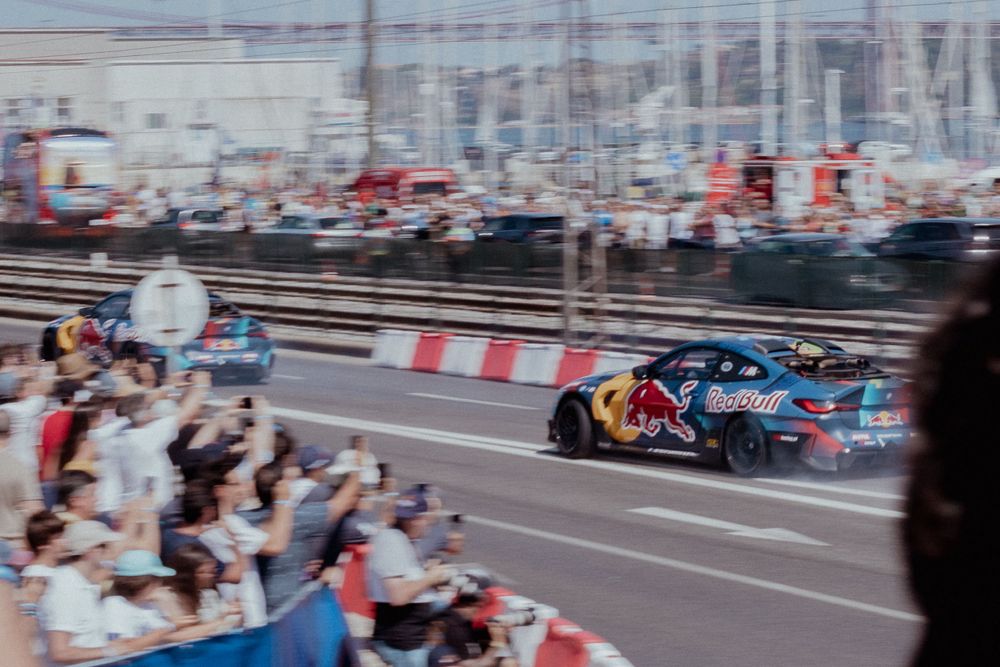Red Bull drift car performing for cheering crowd along street circuit barriers.