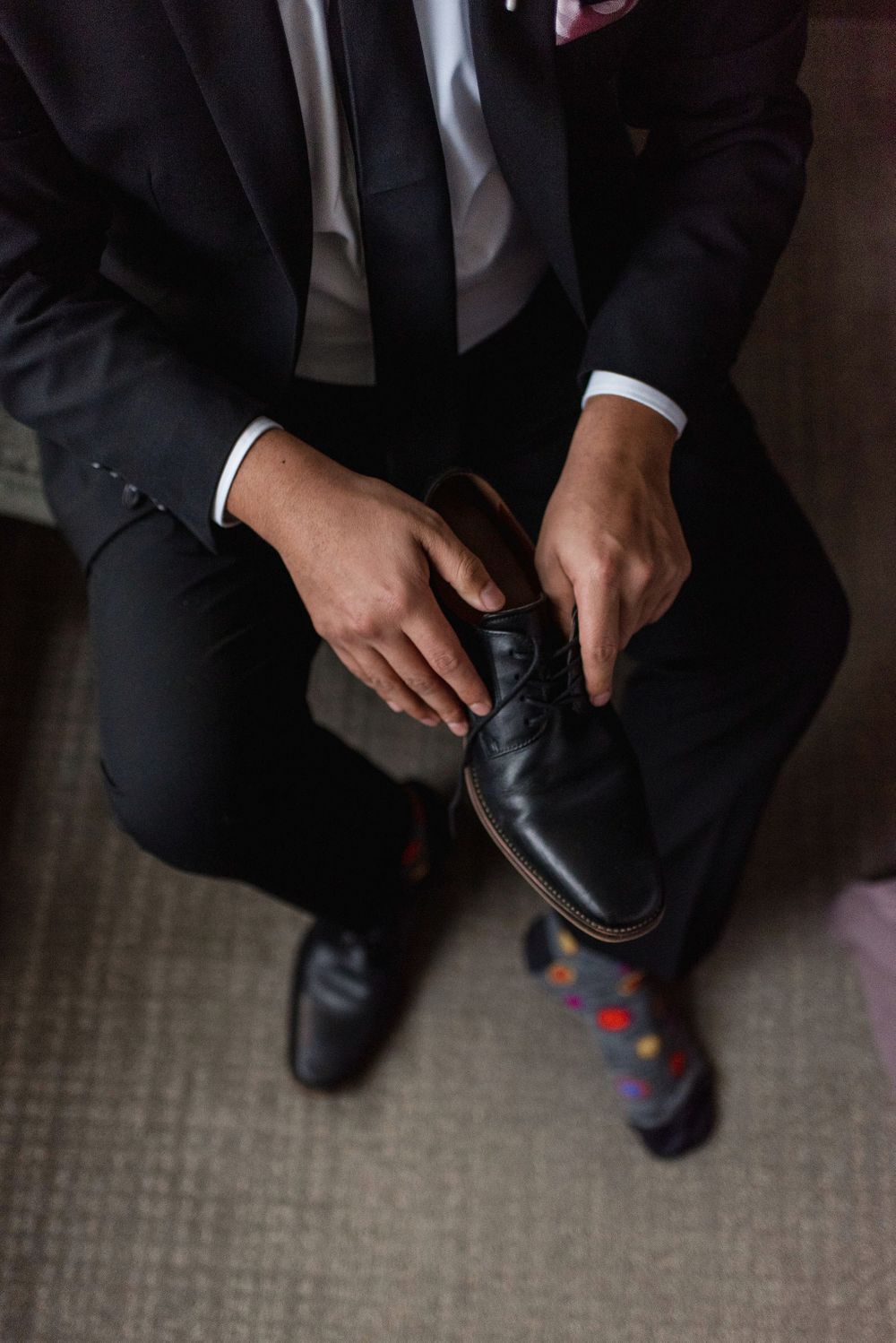 Close-up shot of hands adjusting formal black dress shoes on carpeted floor.
