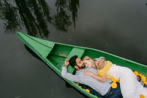 A couple relaxes in a green canoe decorated with yellow flowers on dark reflective water.