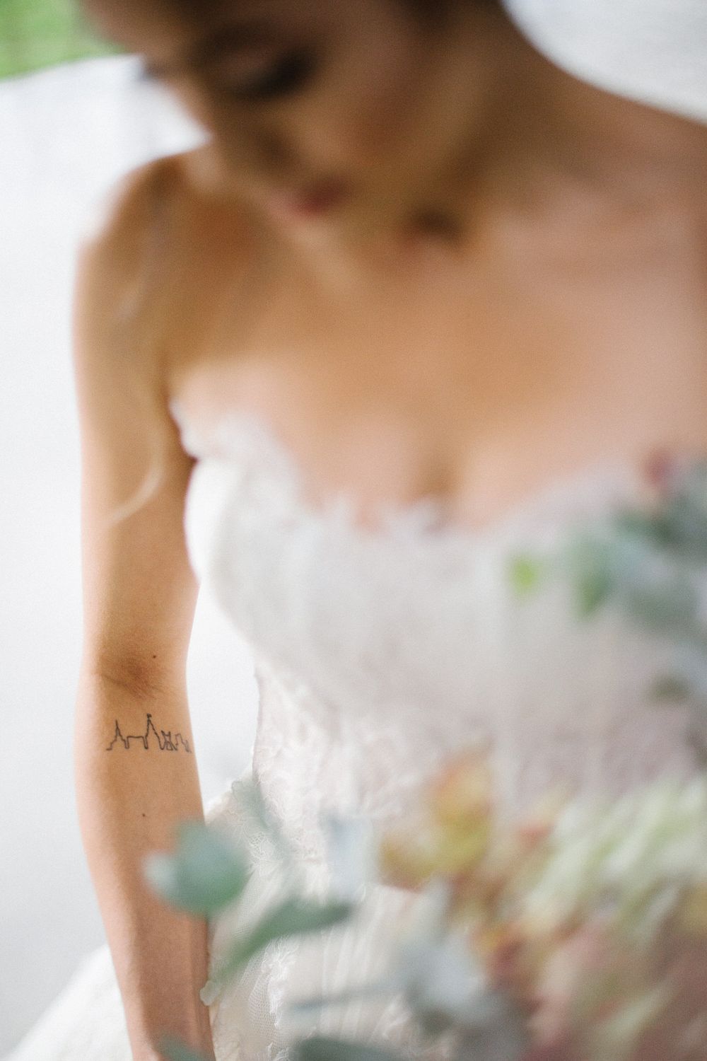Close-up shot of a white lace wedding dress with a delicate heartbeat tattoo visible on the arm.