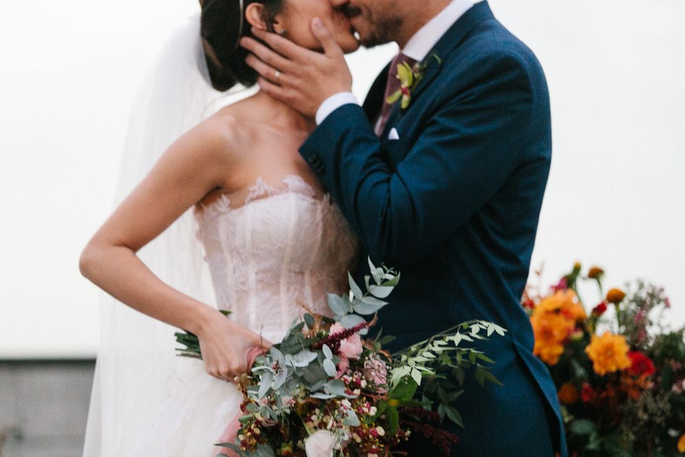 An intimate kiss between newlyweds with a beautiful floral bouquet in hand.